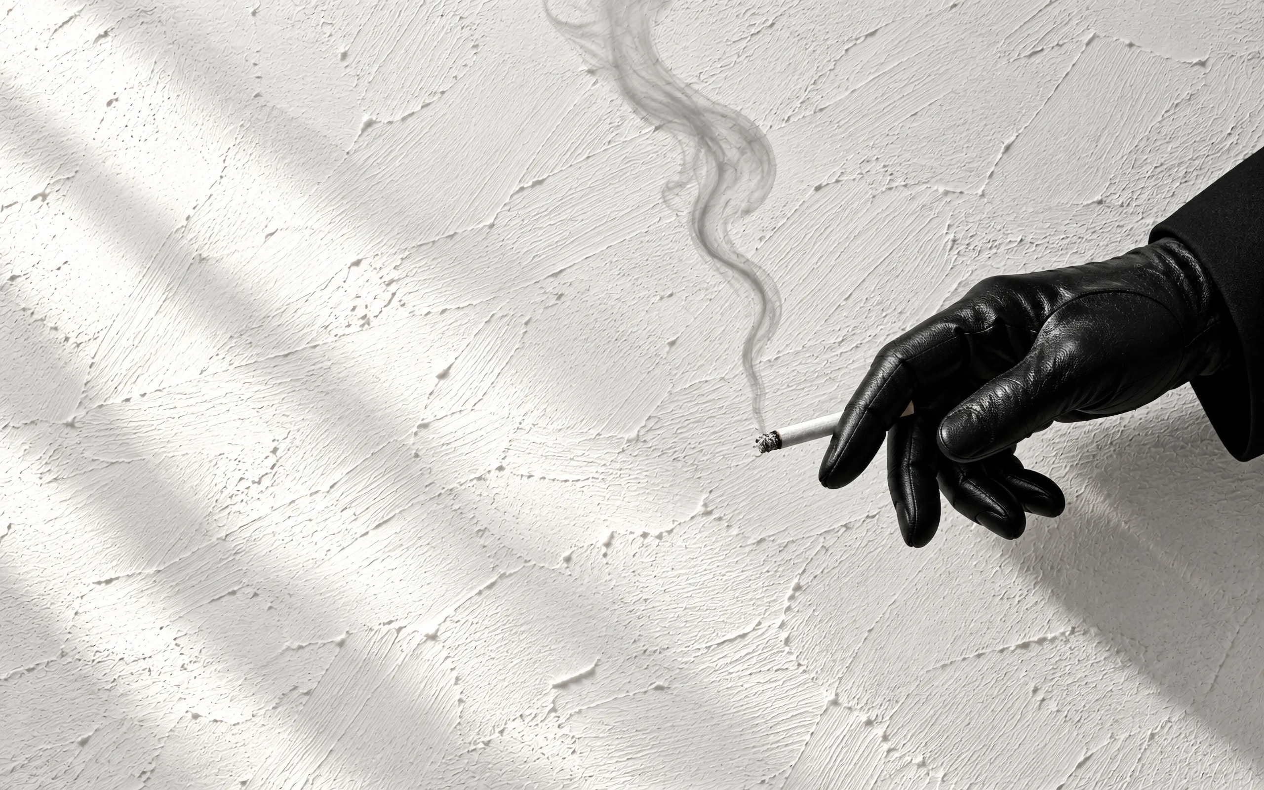 A black-gloved hand holding a cigarette against a sunlit white plaster wall